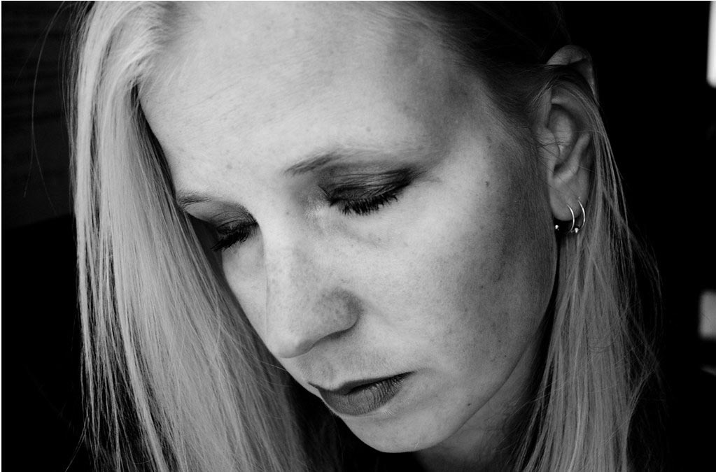Caucasian woman with eyes closed, face pointing down looking sad